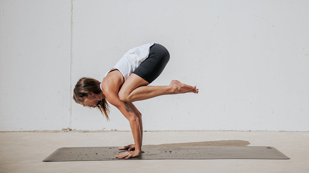 Kobieta wykonująca pozycję kruka (bakasana) w jodze, demonstrująca równowagę i siłę na macie do ćwiczeń