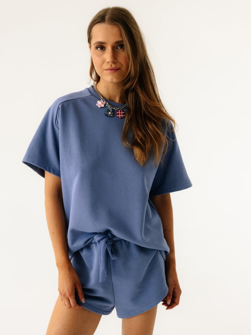 Kobieta prezentuje niebieską bluzę Coast z krótkim rękawem w kolorze Timeless Blue z dopasowanymi szortami